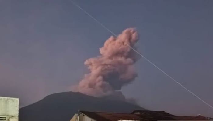 Gunung Marapi Erupsi, Asap tebal berwarna kelabu kecokelatan membumbung dari puncak Gunung Marapi saat erupsi, terlihat jelas dari kejauhan dengan latar langit senja.