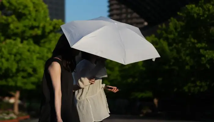 Suhu Ekstrem Picu Peringatan Sengatan Panas di Jepang, Dua perempuan berjalan di bawah sinar matahari menggunakan payung putih untuk berlindung dari panas ekstrem di Tokyo, Jepang.