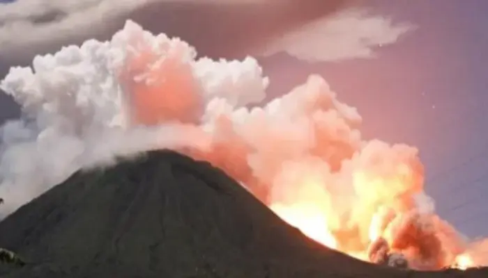 Gunung Lewotobi Kembali Bergejolak, dengan lontaran cahaya pijar dan kepulan asap tebal berwarna putih dan kemerahan di langit senja.