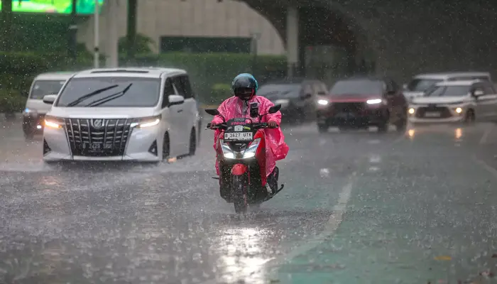 Hujan Ringan Melanda Nusantara, Pengendara motor mengenakan jas hujan melintasi jalanan ibu kota saat hujan deras mengguyur.