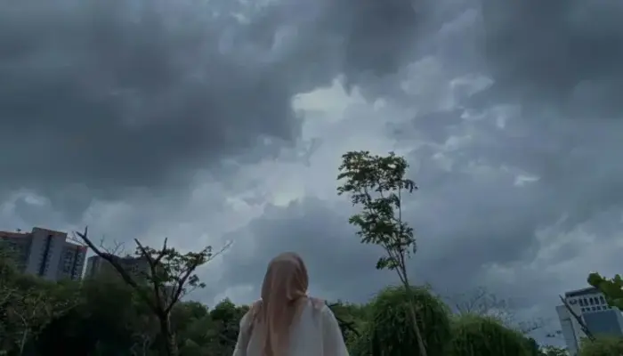 Ancaman Cuaca Ekstrem, Seorang wanita mengenakan kerudung berdiri menatap langit gelap penuh awan mendung tebal sebagai tanda cuaca ekstrem.