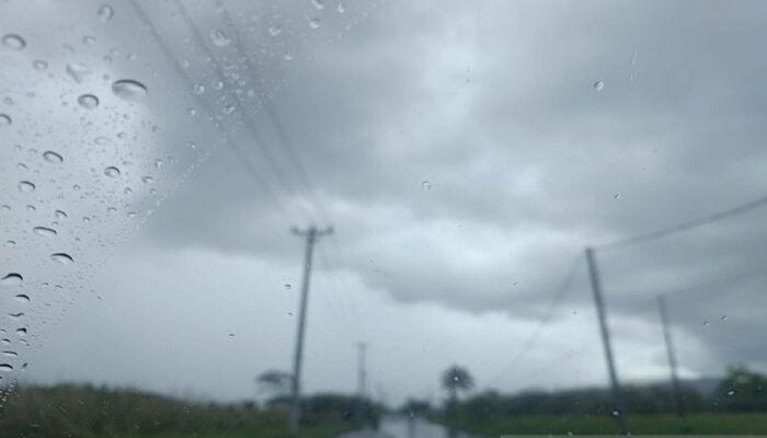Hujan Ringan Sejukkan Kota, Pemandangan jalan pedesaan dengan tiang listrik dan hujan ringan, langit mendung kelabu di Indonesia.