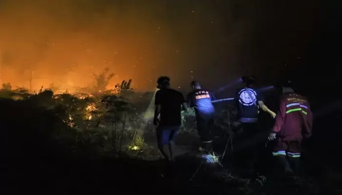 Karhutla Makin Parah, Petugas pemadam kebakaran dan relawan berusaha memadamkan api di tengah kebakaran lahan di Singkawang saat malam hari, dengan latar api yang menyala terang.